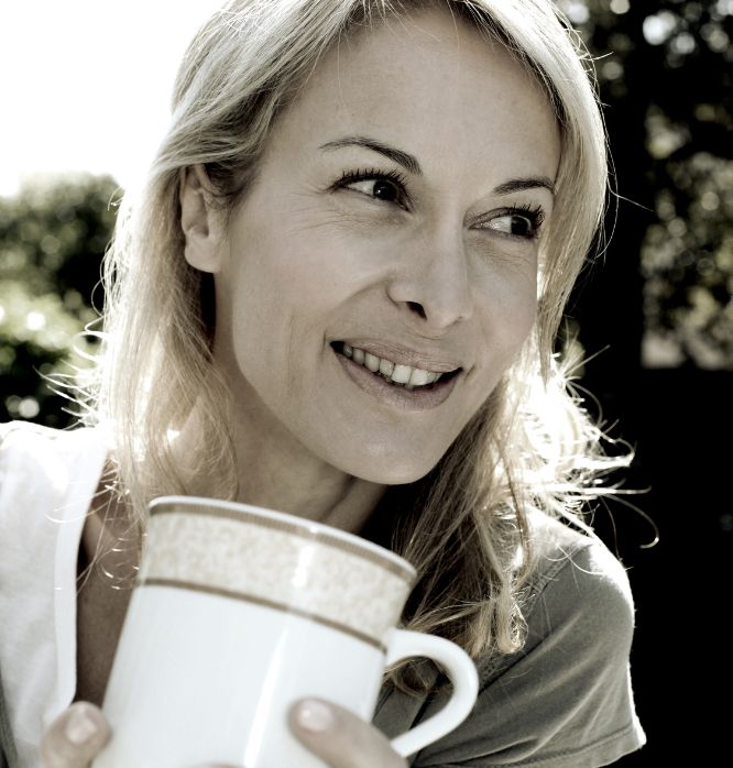 Woman smiling while holding a large coffee mug outdoors, feeling relieved after her successful divorce mediation with Fairway Divorce Solutions.