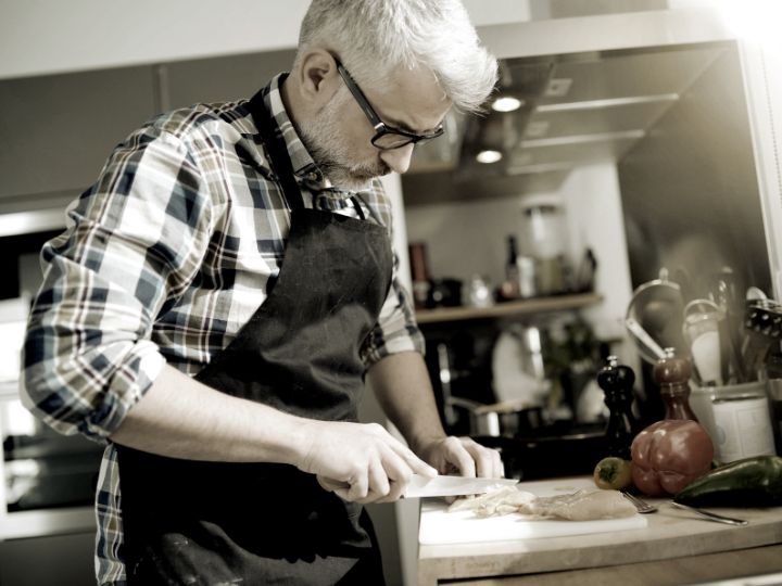 Man with glasses wearing an apron, cutting vegetables in a kitchen, contemplating divorce mediation from Fairway Divorce Solutions.